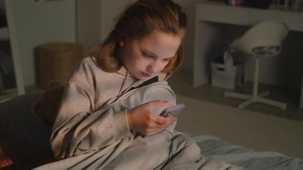 漂亮的小女孩躺在床上 毛绒玩具铺在毯子下 躺在房间里休息 可爱的女学生在晚上用手机滚动社交网络 舒适舒适的家 内部舒适时尚 — 图库视频影像