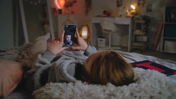 戴耳机的年轻女孩通过视频聊天和哥哥聊天 然后躺在舒适舒适的床上 白种人青少年白天在家里消磨时光 生活方式概念 — 图库视频影像