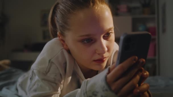 傍晚时分 一个年轻姑娘躺在床上 白人青少年用智能手机上网 并与社交网络上的朋友聊天 迷人的青少年在舒适的卧室度过周末 — 图库视频影像