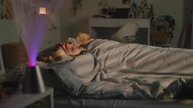 Güzel genç kız battaniyenin altında pelüş oyuncaklarla yatar ve akşamları odasında dinlenir. Sevimli liseli kız uyanıyor ve gece etrafa bakıyor. Rahat bir ev, rahat bir iç mekan..