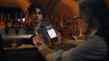 Spor taraftarlarının maç skorlarını ve cep telefonu kullanarak bahisçi reytinglerini kapat. Futbol ligi maçına bahis oynayan bir adam, uygulamayla geceleri barın barında oturuyor. Kumar konsepti.