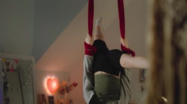Genç kız büyük bir ışık odasının ortasında akrobatik egzersizler yapmak için hava jimnastik kurdeleleri kullanıyor. Kafkasyalı ergen, konfor odasında havadan jimnastik yapıyor. Gençler hafta sonunu evde antrenman yaparak geçirir..