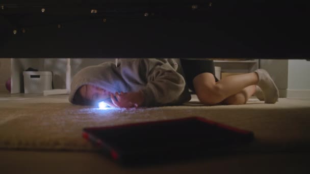 白人のティーンエイジャーは 彼女の携帯電話に懐中電灯で大きなライトベッドルームに来ます 若い女の子はベッドの下にデジタルタブレットのコンピュータを見つけようとし それを取って部屋を出ようとします ベッドの下から撮影 — ストック動画