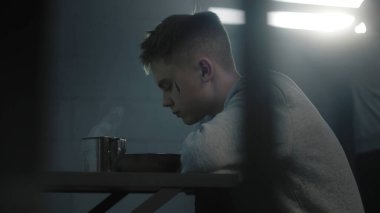 Kafkas ergen mahkum hapishane hücresindeki masada hapishane yemeği yiyor. Genç suçlu, ıslahevinde ya da hapiste suçtan hapis yatıyor. Arka plandaki pencereye bakan başka bir mahkum daha var..