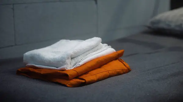 Static shot of prisoner putting orange prison uniform and bath towel on the bed. Guilty criminal or inmate serves imprisonment term in jail. Detention center or correctional facility. Justice system.