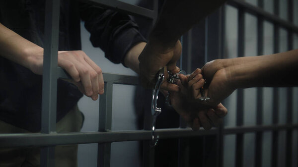 Warden takes off handcuffs from young prisoner. Multi ethnic teenagers serve imprisonment term in correctional facility or detention center. Young inmates in prison cell. Justice system. Close up.