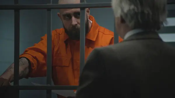 身穿橙色制服的囚犯靠在牢房的铁栏上 与辩护人交谈 阅读律师合同 犯人因犯罪在教养所服刑 Gangster Detention Centre — 图库照片