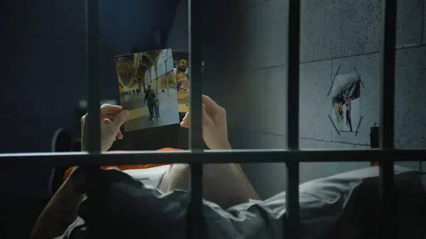 男性の囚人は刑務所のベッドに横たわり 家族の写真を見ている 同性愛者または犯罪者は刑務所で犯罪の刑期を定めている 金属棒を通して見る 拘禁センターまたは矯正施設 — ストック写真