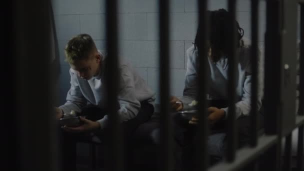 两名多族裔少年囚犯坐在牢房的床上 吃铁碗里的食物 年轻罪犯因在狱中犯罪而服刑 青少年拘留中心或教养所 — 图库视频影像
