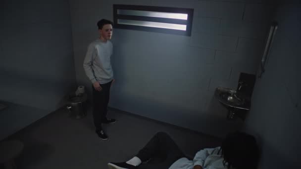 不同的青少年在服刑期间交谈 年轻的白种人囚犯站在监牢的窗前 非洲裔美国人囚犯坐在床上 少年拘留中心 监视摄像头 — 图库视频影像