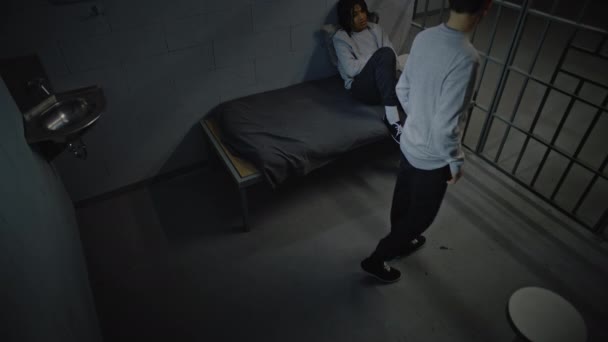 两名不同的青少年囚犯谈论在狱中服刑的问题 一个在监牢里走来走去 另一个坐在床上 少年拘留中心或教养所 闭路电视摄像角度 — 图库视频影像