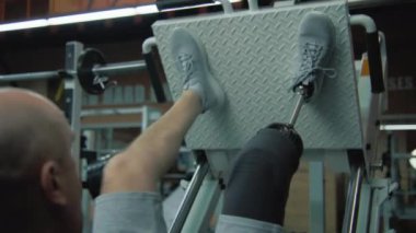 Modern spor salonunda protez bacaklı sporcu bacak pres makinesinde. Fiziksel engelli aktif atletik adam spor malzemelerini kullanarak egzersiz yapıyor. Vücut pozitif konsept.