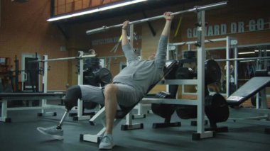 Modern fitness merkezinde boş halterli protez bacak egzersizleri yapan yetişkin bir sporcu. Fiziksel engelli motive bir sporcu profesyonel spor ekipmanları kullanarak güçlü bir antrenman yapıyor..