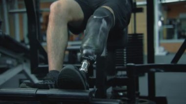 Motivasyonlu sporcu, modern fitness odasında ya da spor salonunda bacak trenleri ve egzersiz makineleri üzerinde protez kullanıyor. Fiziksel engelli yetişkin bir sporcu profesyonel spor malzemelerini kullanarak antrenman yapıyor..