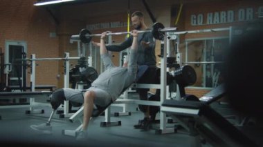 Protez bacaklı atletik bir adam spor salonunda halterle ağırlık antrenmanı yapar, fitness terapisi antrenörüyle, sonra da ara verir. Yapay bacaklı sporcu spor malzemelerini kullanarak egzersiz yapıyor..