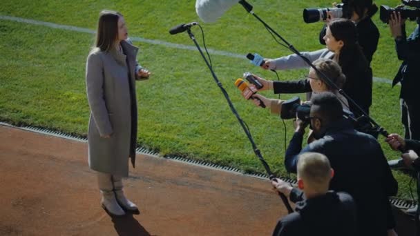 サッカーチームのディレクターがプレス質問に答え 試合前にサッカー場の近くでインタビューを行いました 女性の民間投資家はニュースジャーナリストに混乱した 記者会見におけるインスピレーションスピーチ — ストック動画