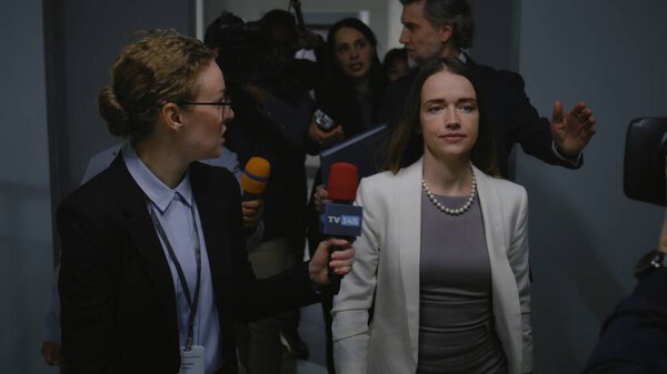 Busy female American minister talks with TV press about hot button issues, gives interview to the media walking in hallway of government building. Politician surrounded by crowd of news journalists.