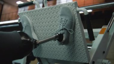 Modern spor salonunda ya da fitness merkezinde bacak pres makinesi üzerinde egzersiz yapan protez bacaklı sporculara yakın çekim. Fiziksel engelli formda bir adam profesyonel spor malzemelerini kullanarak antrenman yapıyor..