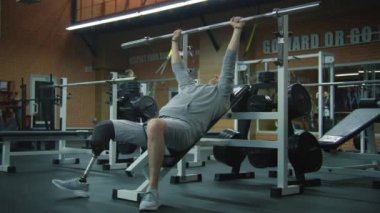 Modern fitness merkezinde boş halterli protez bacak egzersizleri yapan yetişkin bir sporcu. Fiziksel engelli motive bir sporcu profesyonel spor ekipmanları kullanarak güçlü bir antrenman yapıyor..