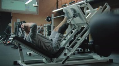 Modern fitness merkezinde bacak pres makinesinde protez bacaklı motive bir sporcu. Yapay bacaklı yetişkin sporcu profesyonel spor aletleri kullanarak güç egzersizleri yapıyor..