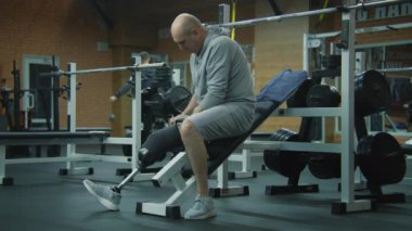 Protez bacaklı motive bir sporcu protezi düzeltir ve modern spor salonunda boş halterle antrenman yapmaya başlar. Fiziksel engelli formda bir adam profesyonel spor malzemelerini kullanarak egzersiz yapar..