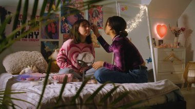 Afrikalı Amerikalı kız sevimli Asyalı arkadaş yüzüne makyaj yapıyor. İki çok kültürlü genç kız yatak odasında oturup birlikte eğleniyorlar. Şık bir iç dekorasyonu olan rahat bir ev. En iyi arkadaş ilişkisi