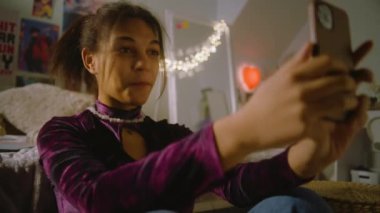Güzel genç, odasında yatağın yanında oturuyor ve telefonla fotoğraf çekiyor. Afrikalı Amerikalı kız arkadaşlarıyla sohbet ediyor ya da blog içeriği yaratıyor. Rahat bir evde boş vakit geçirmek..