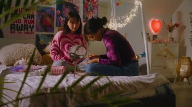 Afrikalı Amerikalı kız sevimli Asyalı arkadaş yüzüne makyaj yapıyor. İki çok kültürlü genç kız yatak odasında oturup birlikte eğleniyorlar. Şık bir iç dekorasyonu olan rahat bir ev. En iyi arkadaş ilişkisi