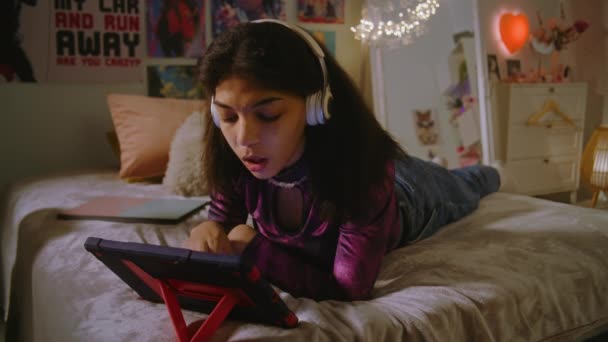 Hermosa Adolescente Los Auriculares Encuentra Cama Habitación Utiliza Una Tableta — Vídeo de stock