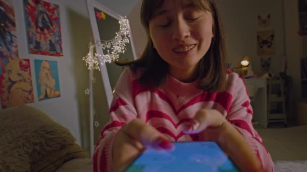 亚洲女孩在网上用智能手机与好友聊天 微笑着躺在舒适的卧室床上 十几岁的女孩放学后在家里消磨时光 近景宽拍 — 图库视频影像