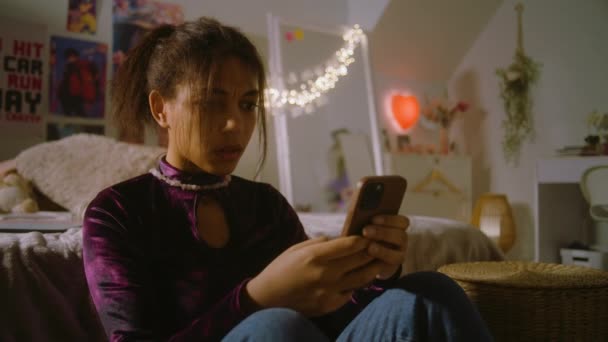 十几岁的少女坐在靠近床边的地板上 在房间里尖叫着 在电话里情绪化地打字 愤怒的非洲裔美国女孩通过电话交流 待在家里的闲暇时间 有时尚室内装潢的家 — 图库视频影像