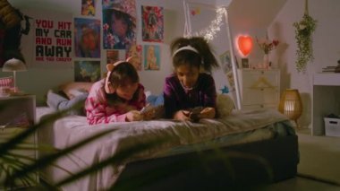 Yatak odasında çok ırklı iki genç kız, internette akıllı telefonlarıyla gezinip kulaklıkla müzik dinlerken konuşup gülüyorlar. En iyi arkadaşlar evde birlikte eğleniyor. Yatakta uzanıyorlar..
