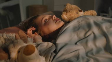 Güzel genç kız battaniyenin altında pelüş oyuncaklarla yatar ve akşamları odasında dinlenir. Sevimli liseli kız uyanıyor ve gece etrafa bakıyor. Rahat bir ev, rahat bir iç mekan..