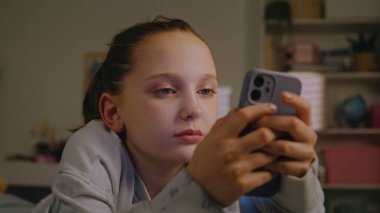 Kafkasyalı gencin sosyal ağlardaki arkadaşlarıyla sohbet etmek ve internette sörf yapmak için cep telefonunu kullanmasına yakın çekim. Genç kız aydınlık yatak odasında rahat yatağında yatıyor. Gençler hafta sonunu evde geçirir..