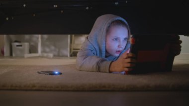 Genç kız cep telefonunda el feneriyle büyük ışıklı yatak odasına gelir. Kafkasyalı genç yatağın altına girer, dijital tablet bilgisayarı bulur ve kullanır. Yatağın altından ateş ediyor. Yaşam tarzı kavramı.