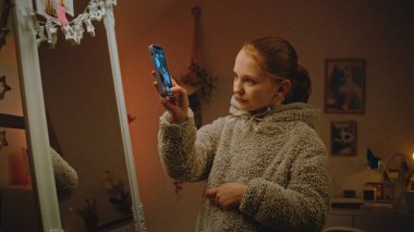 Genç, güzel bir kız yatak odasında aynanın önünde makyaj yapıyor, sonra da telefonla fotoğraf çekiyor. Kafkasyalı genç akşamları boş vakitlerini evde geçiriyor. Yaşam tarzı kavramı.