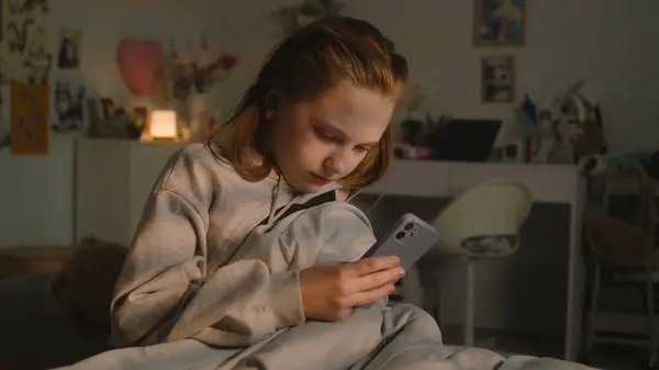 白人青少年一大早就在她舒适的卧室里起床了 小女孩拿起她的手机 关掉了闹钟 青少年坐在舒适的床上 用她的智能手机在社交网络上聊天 — 图库照片