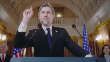 Olgun ABD bakanı veya politikacı Beyaz Saray 'daki basın toplantısında konuştu. Birleşik Devletler Başkanı ilham verici bir konuşma yapıyor, sonra da kameralara poz veriyor. Arka planda Amerikan bayrakları.