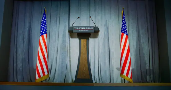 Stock image Tribune for politician, congressman or US minister political speech in the White House in press campaign room. Wooden conference debate stand with microphones on stage. American flags in background.