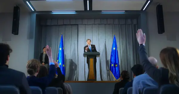 stock image Confident politician makes an announcement, answers media questions and gives interview. Mature representative of the European Union during performance at press conference. Backdrop with EU flags.