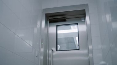 Cerrah koridor boyunca yürür ve otomatik temassız kapı açma mekanizmasıyla otomatik demir modern kapılardan ameliyathaneye girer.