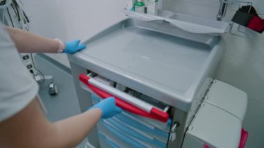 Bir hemşire ameliyathanede ameliyat hazırlarken içinde ilaç tabletleri ve uyuşturucular bulunan bir sehpayı açar..