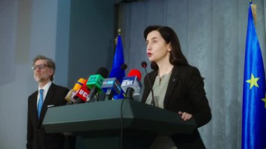 Kadın siyasetçi bir duyuru yapıyor, gazetecilere sorular soruyor ve medyaya röportaj veriyor. Basın toplantısı sırasında Avrupa Birliği 'nin kendinden emin temsilcisi. AB bayraklı arkaplan.
