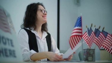 Kadın anket memuru oy merkezindeki masada oturuyor, oy verdikten sonra seçmenlere Amerikan bayrağı ya da rozeti veriyor. Amerika Birleşik Devletleri 'nde Ulusal Seçim Günü. Vatandaşlık görevi ve demokrasi.