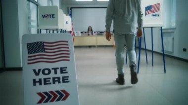 Afrika kökenli Amerikalı bir adam, erkek seçmen oy kullanma merkezinde kayıt olmak için kadın sandık görevlisine gider, oy vermek için kağıt oy kullanır. Amerika Birleşik Devletleri 'nde Ulusal Seçim Günü. Yurttaşlık görevi.