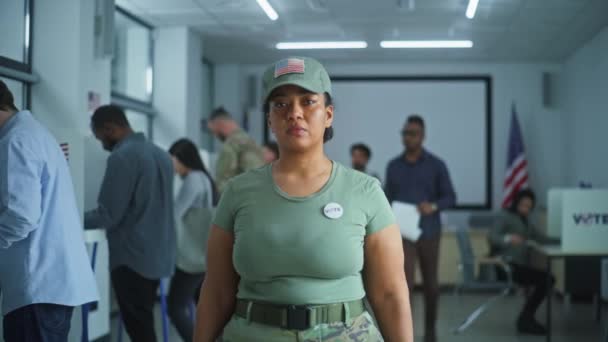 カモフラージュのユニフォームの女性は ポーリングステーションに立って カメラを見ています 女性兵士の肖像画 アメリカ合衆国選挙の有権者 投票ブースの背景 市民の義務に関する概念 — ストック動画
