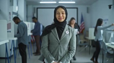 Kadın modern bir seçim merkezinde duruyor, poz veriyor, gülümsüyor ve kameraya bakıyor. Arap kadın portresi, Amerika Birleşik Devletleri seçmeni. Oy verme kabinleri olan bir arka plan. Yurttaşlık görevi kavramı.