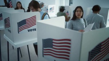 Asyalı kadın oy kullanma merkezindeki kabine oy vermeye geliyor. Birleşik Devletler 'de Ulusal Seçim Günü. ABD başkan adaylarının siyasi ırkları. Vatandaşlık görevi kavramı. Ağır çekim. Dolly vurdu..