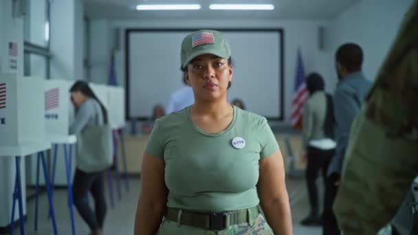 女兵的画像 美利坚合众国选举选民 身着迷彩服的妇女站在投票站 看着镜头 有投票亭的背景 公民义务的概念 — 图库视频影像