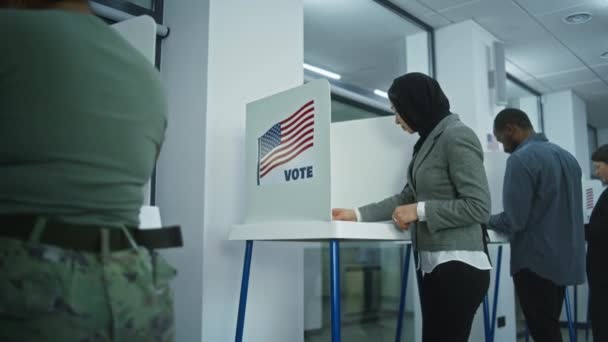 ヒジャブのムスリム女性は 投票所のブースで投票に来ます アメリカ合衆国の国民選挙の日 アメリカ合衆国大統領候補の政治的競争 市民の義務に関する概念 ドリー ショット — ストック動画